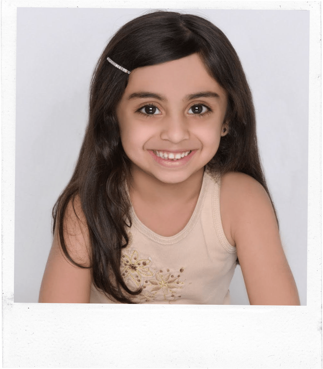 A headshot of a girl, aged 5-6, wearing a light brown tank top smiling. 