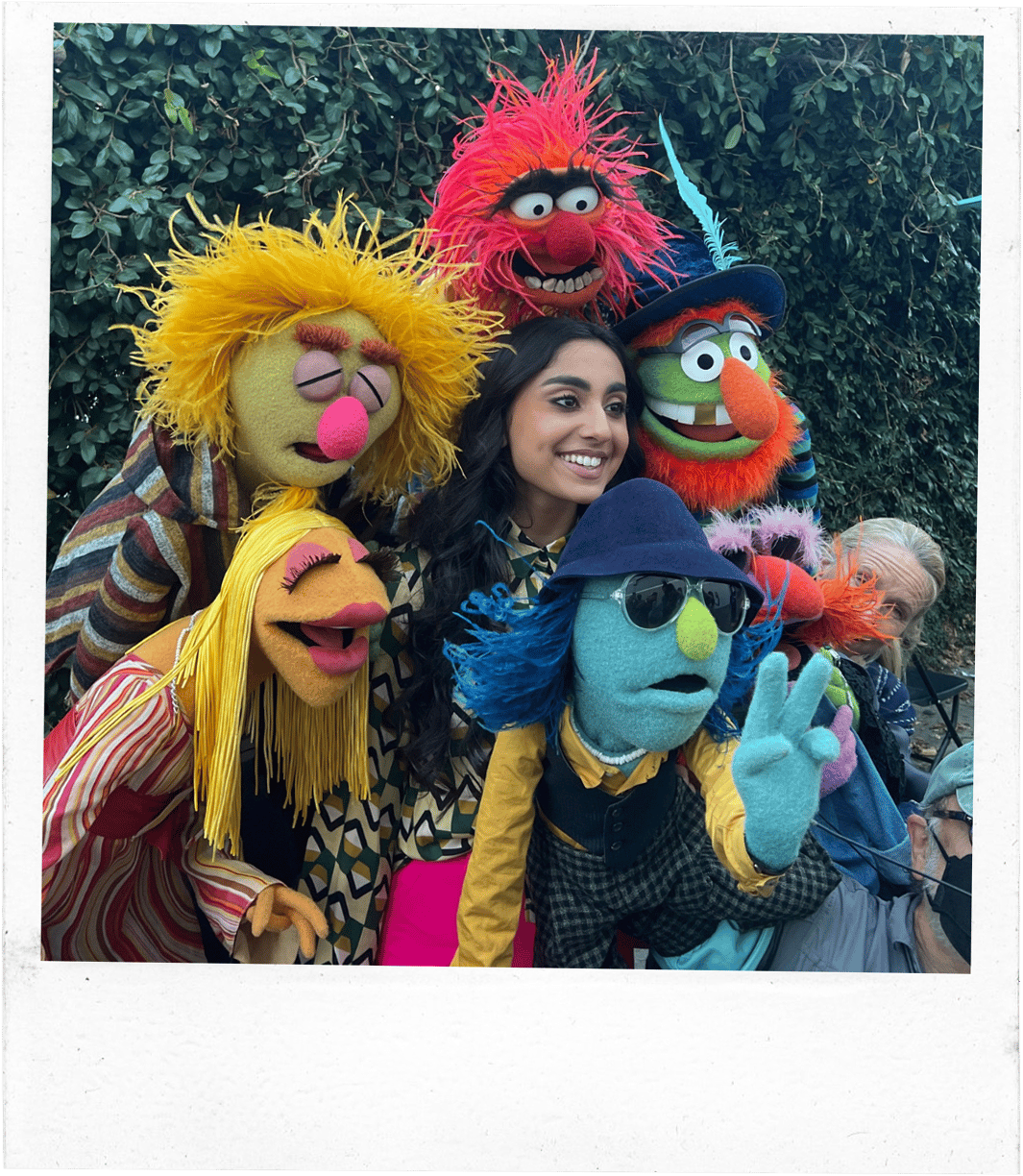 A girl smiles as she is surrounded by 5 colourful puppets
