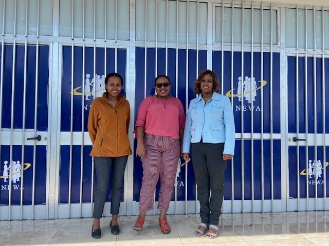 Three women staff members of the Network of Ethiopian Women’s Association stand together outside their building.