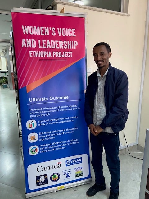 Kassahun Getahun, a grant coordinator with Plan International Ethiopia, stands next to a sign with the text: “Women’s Voice and Leadership Ethiopia project.”