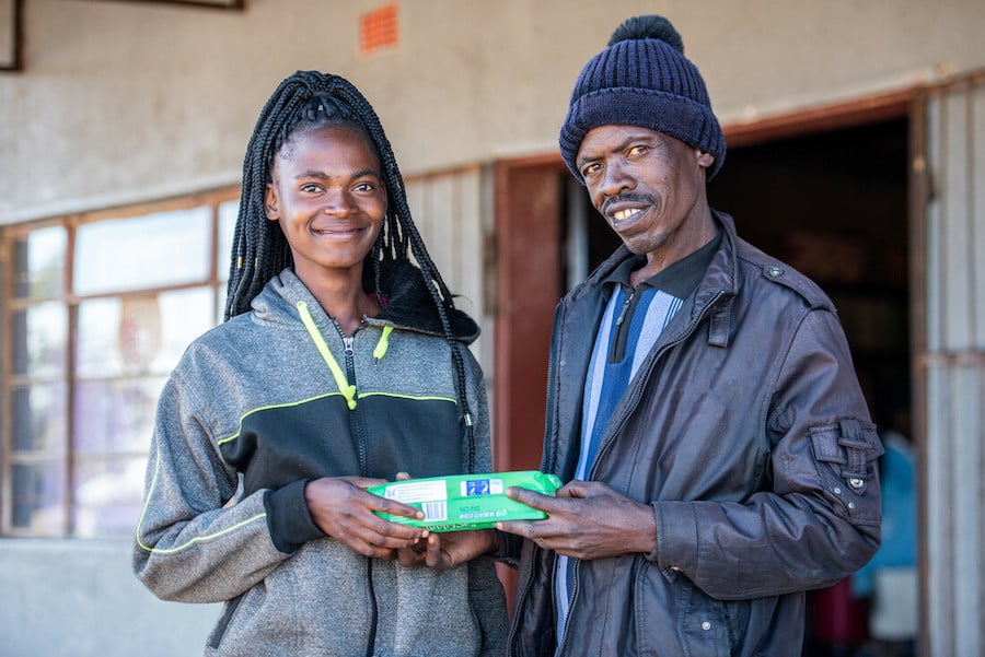 Young woman and her father in Zimbabwe hold a package of menstrual pads and smile.