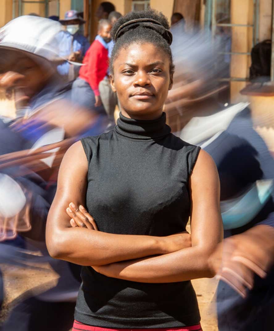 Tanyaradzwa, arms crossed in front of a busy background