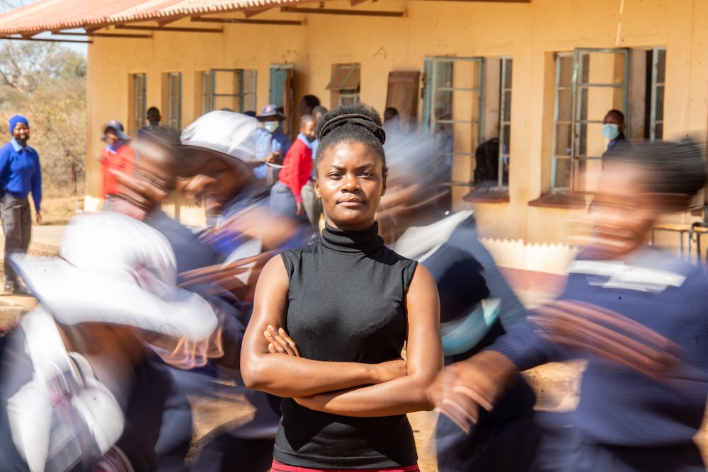 Photographer captures young woman standing still with arms crossed amid blurred movement of others in motion.